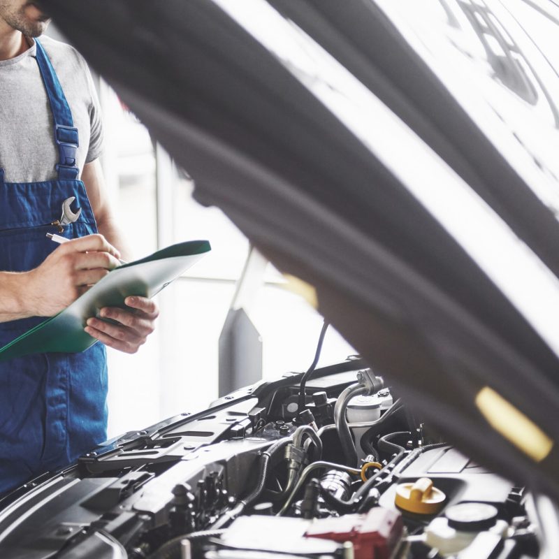 Portrait of a mechanic at work in his garage - car service, repair, maintenance and people concept.